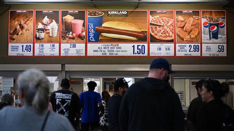 Customers wait in line to order below signage for the Costco Kirkland Signature $1.50 hot dog and s...