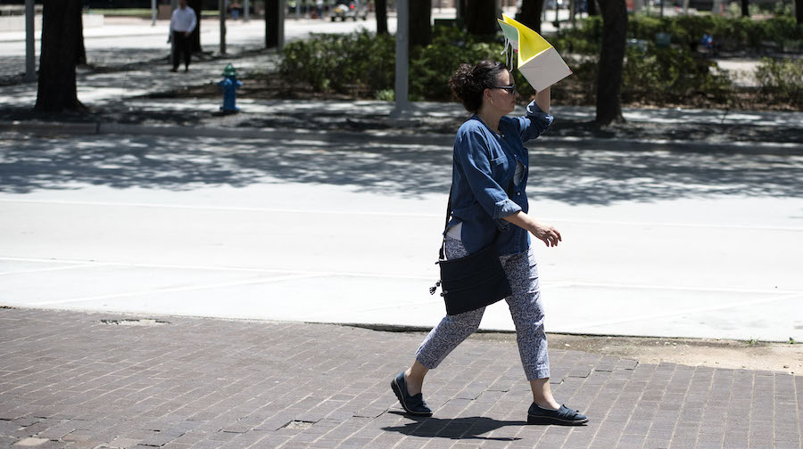 A pedestrian walks with a bag covering her face to block the sun during a heatwave in Houston, Texa...