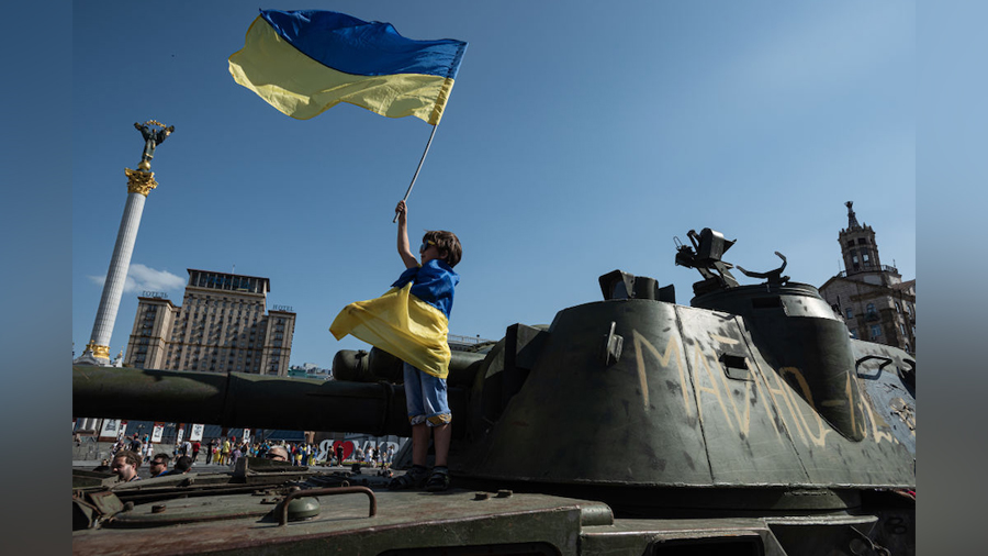 A boy wrapped in Ukrainian national flag holds a Ukrainian national flag as he stands on top of a R...