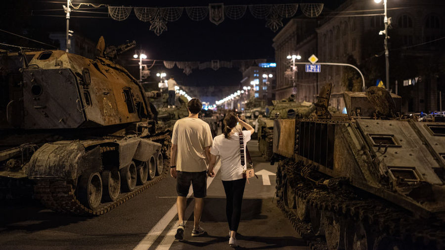 A couple walks by burnt-out Russian military vehicles displayed in the downtown area on August 22, ...