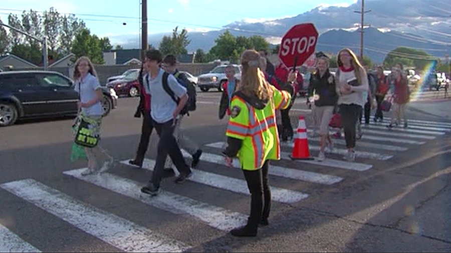 Students cross the street with a crossing guard holding traffic (KSl TV)...