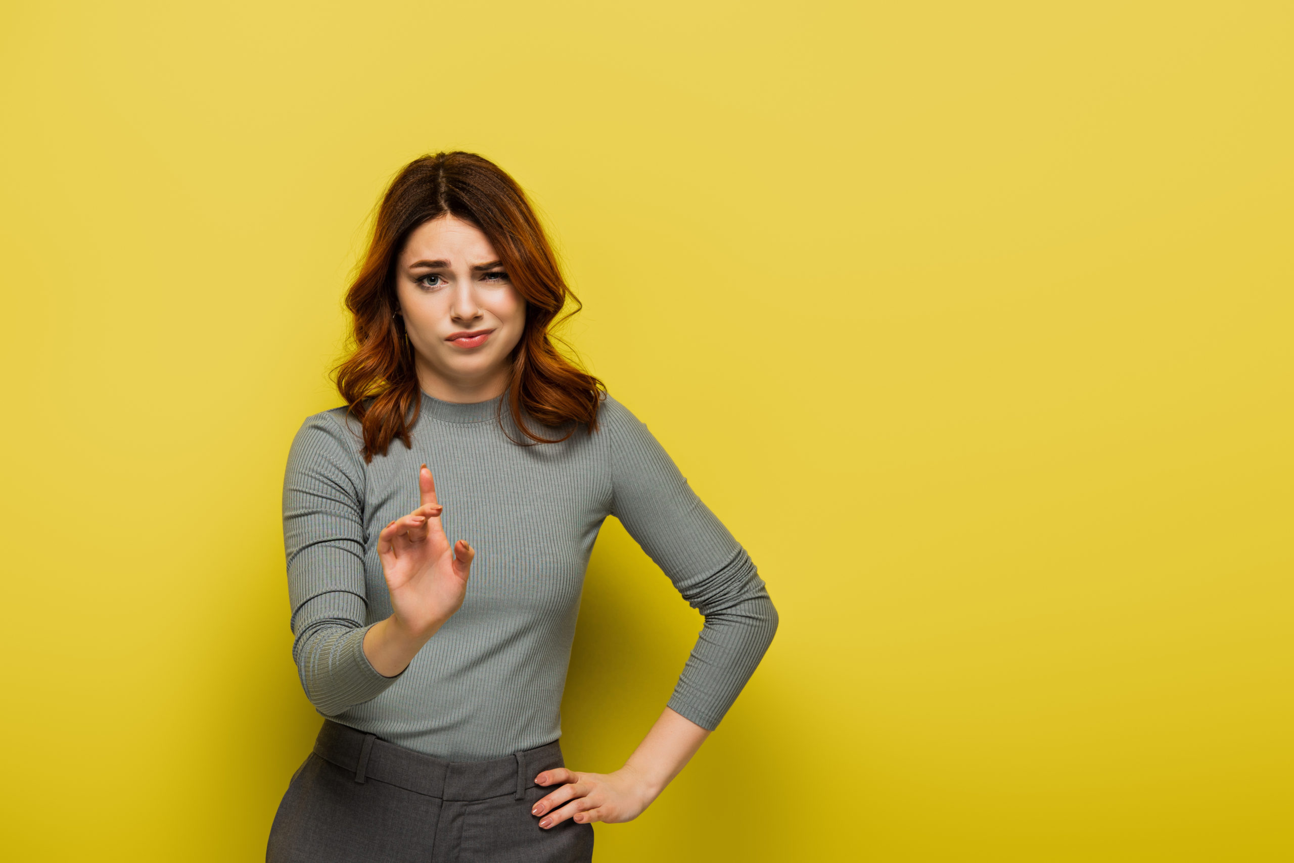 displeased woman standing with hand on hip and pointing with finger while showing no sign on yellow
