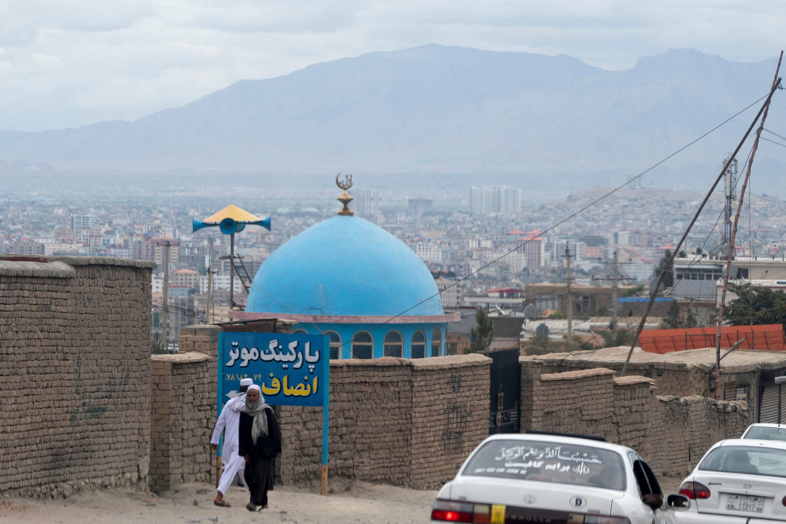 Afghan men walk past the blue dome of a mosque a day after the blast in the outskirts of Kabul on A...