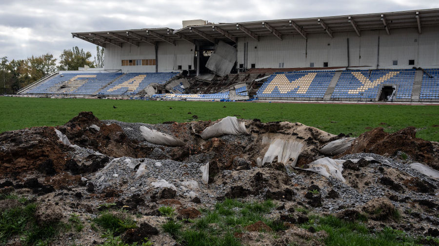 A missile crater pierces a football pitch near a spectator stand that has also been struck by a mis...