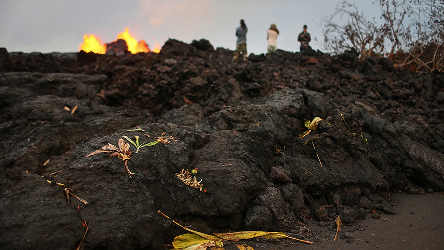 Onlookers stand on hardened lava from a Kilauea volcano fissure as lava erupts in Leilani Estates, ...