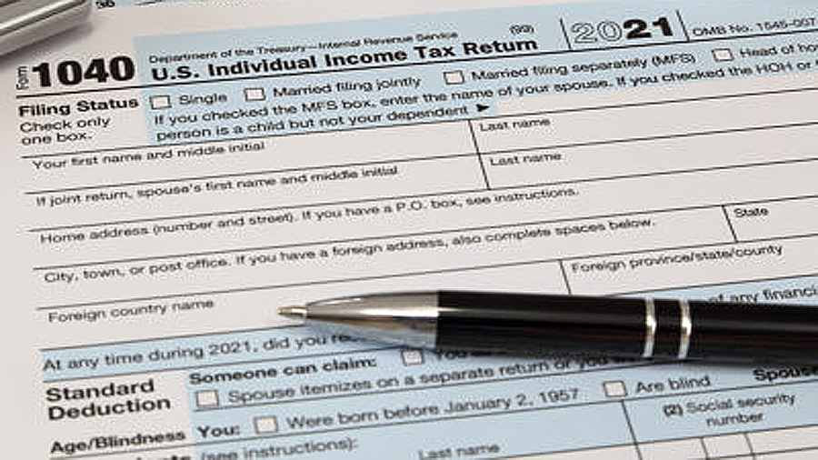 An IRS 1040 tax year 2021 form is shown in 2022, along with an ink pen, calculator, and glasses. Th...