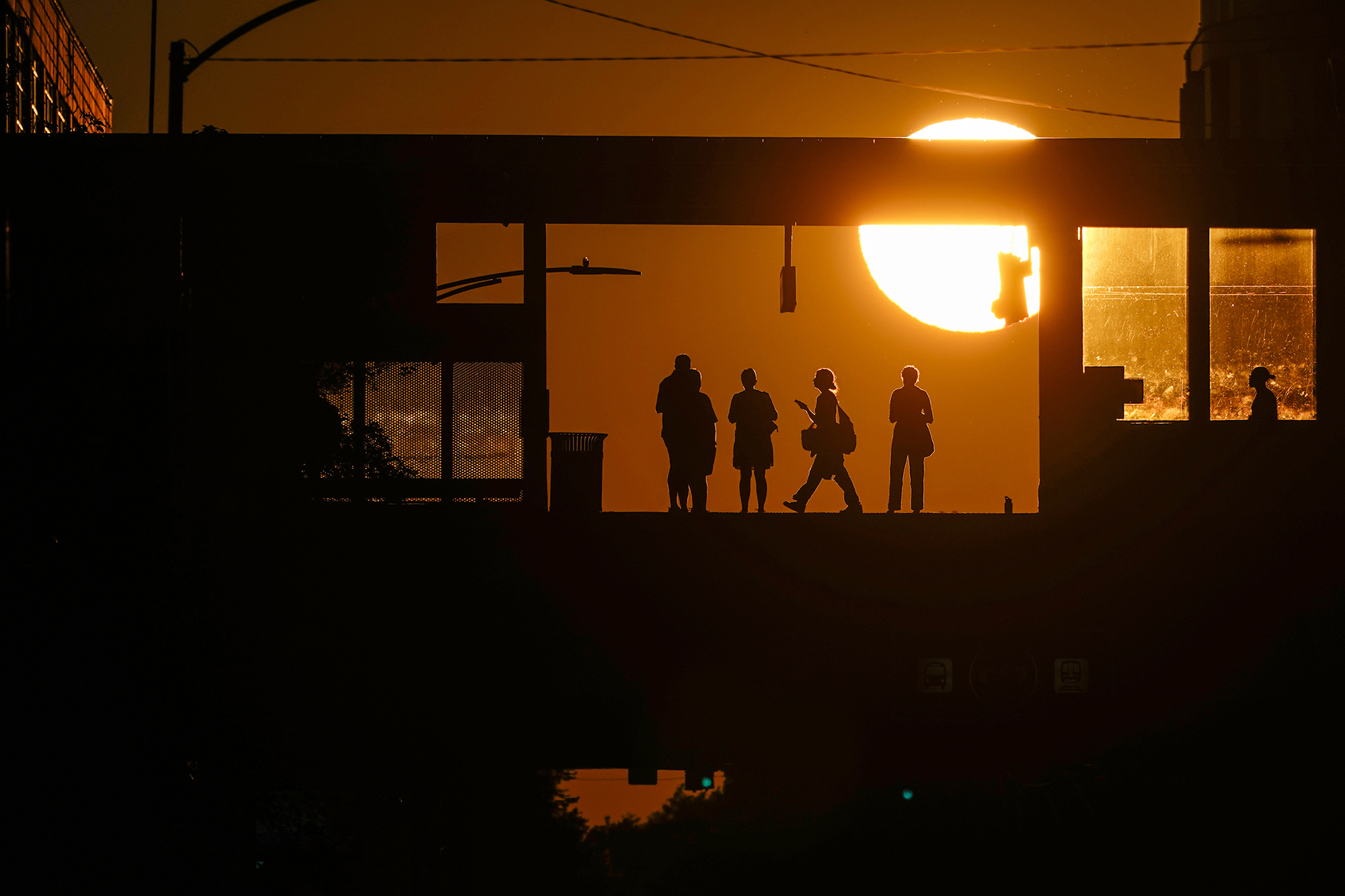 Commuters waiting for Chicago's L Train are silhouetted against the setting sun at Addison Station,...