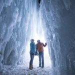 Two people look up at the icicles in a trench between two walls of ice. (AJ Mellor, Ice Castles)