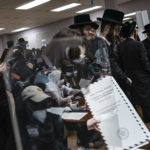 Poll workers are seen in a reflection while members of the Orthodox Jewish community register to collect ballot papers at a polling center on, Tuesday, Nov. 8, 2022, in the Brooklyn borough of New York. (AP Photo/Wong Maye-E)