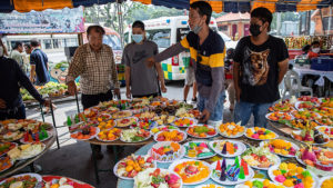 People preparing several plates of colorful fruits.