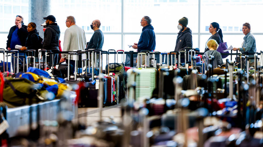 Travelers wait in line before they are allowed to search for their luggage in a baggage holding are...