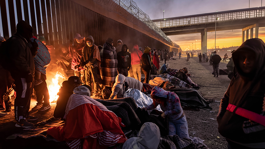 Immigrants warm to a fire at dawn after spending the night outside next to the U.S.-Mexico border f...