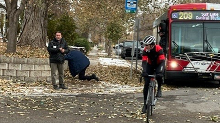 A cyclist is riding his bike away from a bus, whose driver is on the ground....