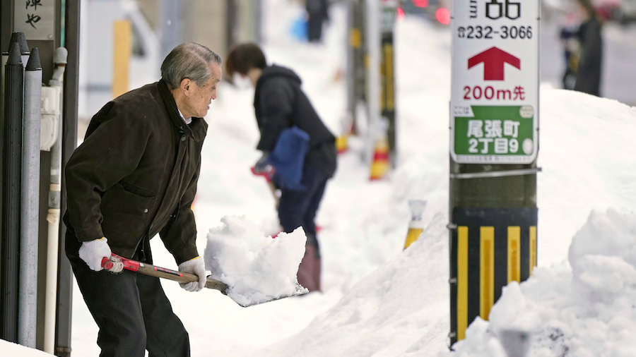 Residents shovel snow off a sidewalk in Kanazawa, Ishikawa prefecture, central Japan, on December 2...