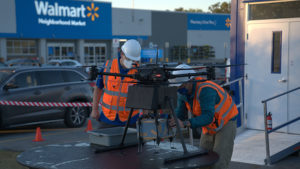 drone pilots load a package onto a drone outside of a walmart store