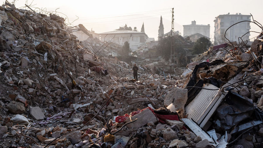 A man walks in the debris of a collapsed building as he awaits news of loved ones on February 13, 2...