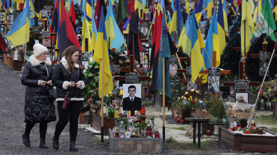 Women walk among fluttering flags and the graves of dead Ukrainian soldiers at the Field of Mars ce...