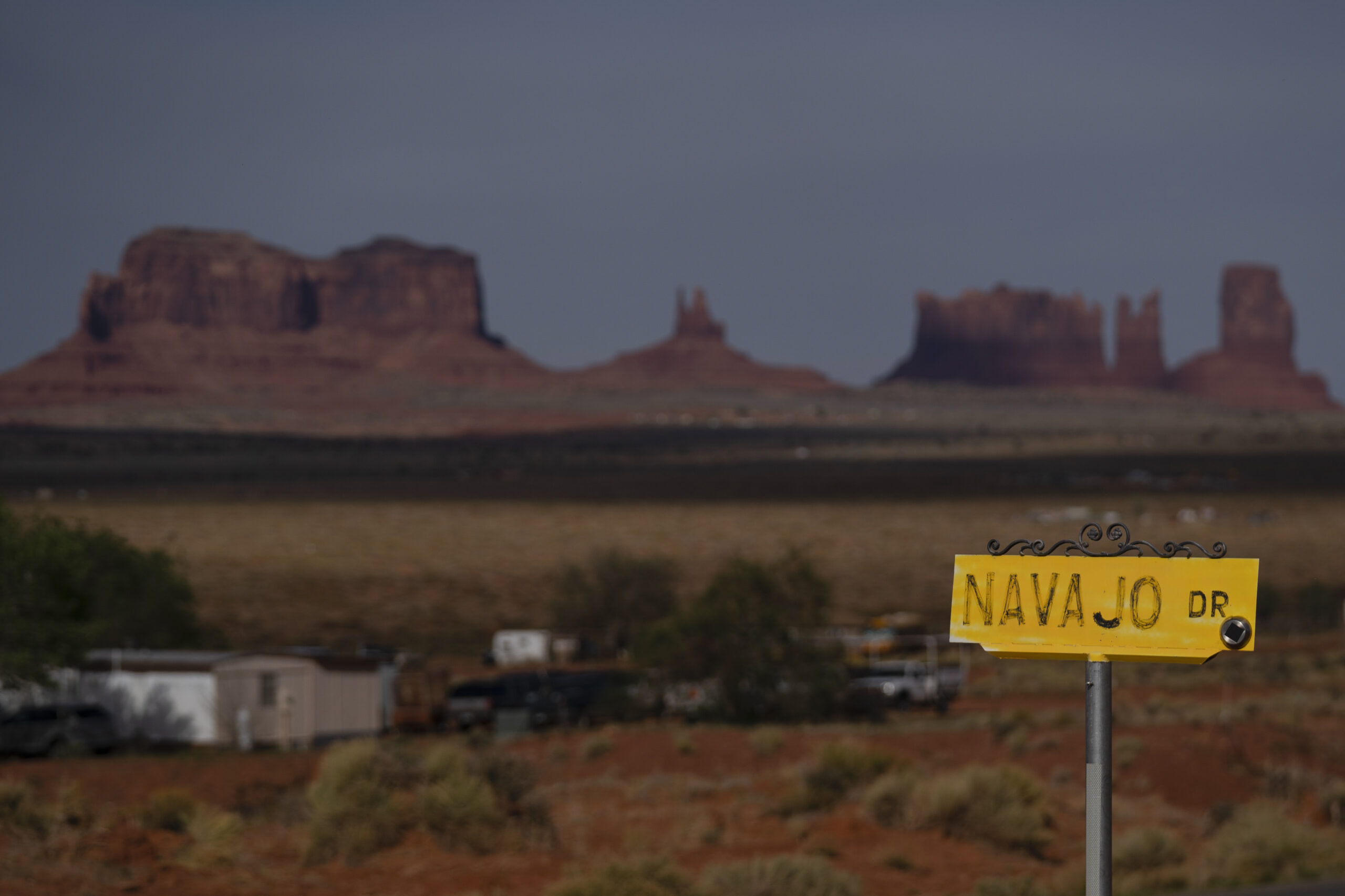 FILE - A sign marks Navajo Drive, as Sentinel Mesa, homes and other structures in Oljato-Monument V...