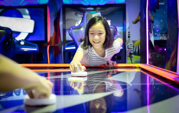 Asian little girl playing arcade game on the computer machines at the shopping mall outlets