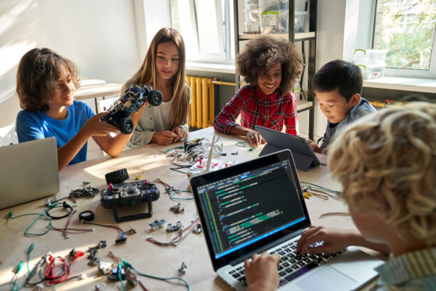 Diverse school children students build robotic cars using computers and coding.