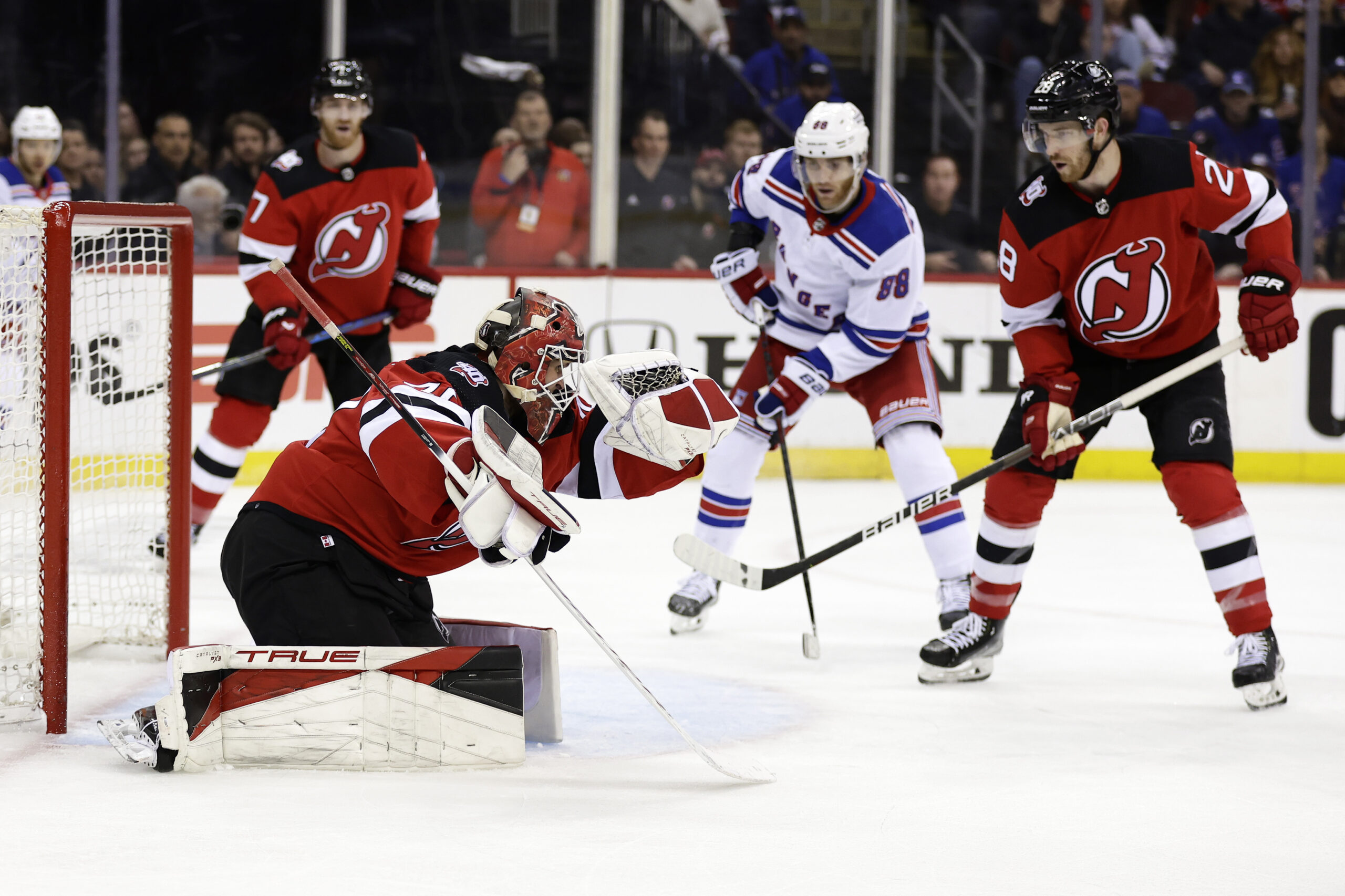 New Jersey Devils goaltender Akira Schmid, front left, makes a save in front of New York Rangers ri...