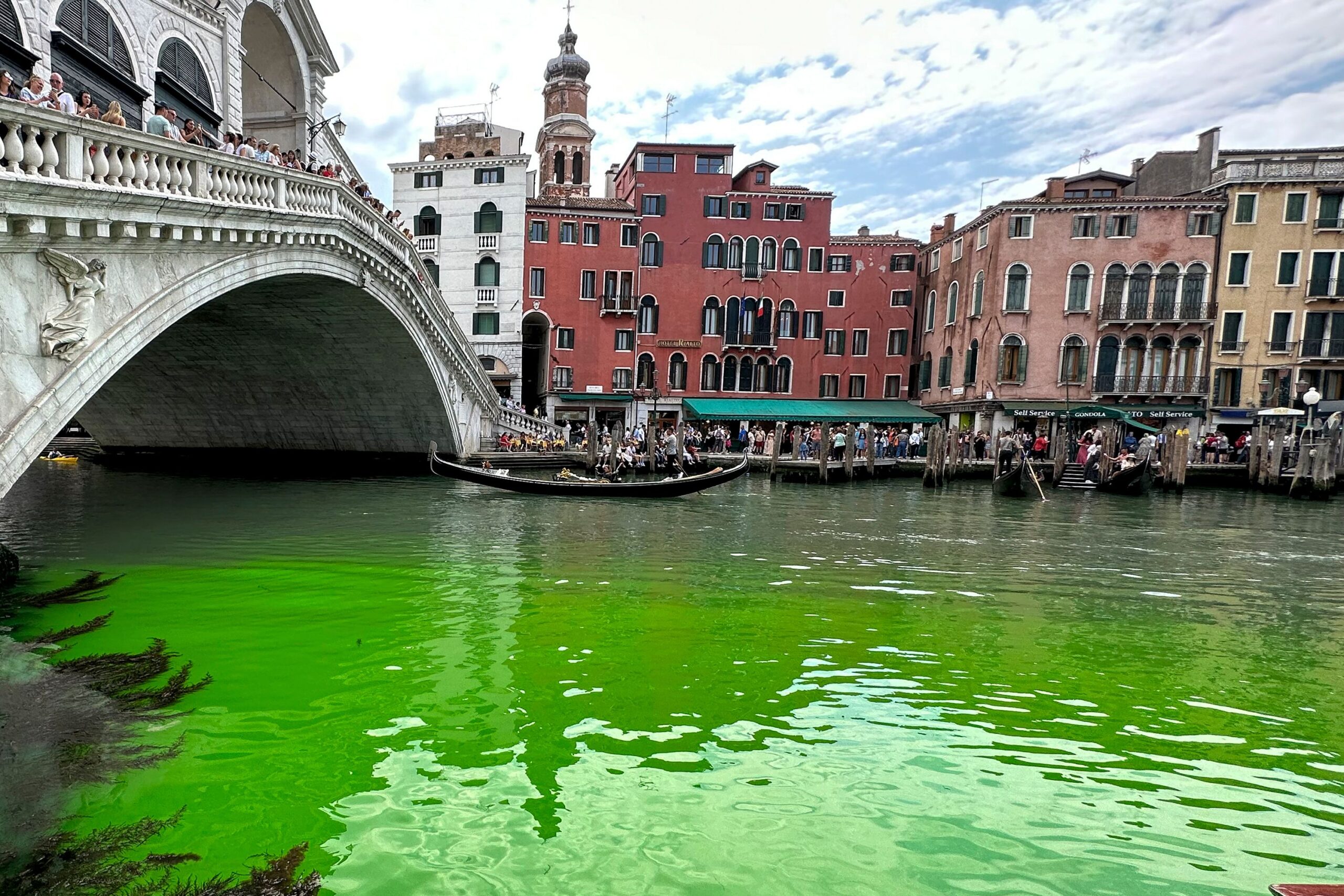Gondolas navigate by the Rialto Bridge on Venice's historical Grand Canal as a patch of phosphoresc...