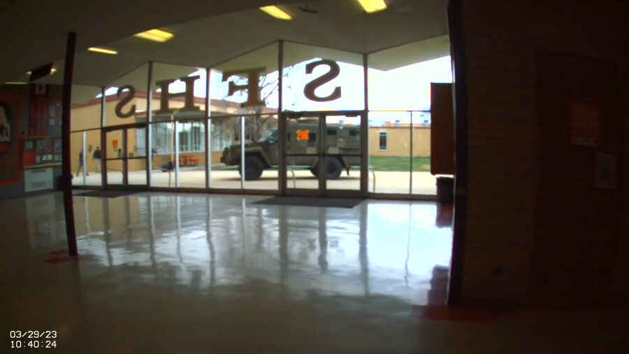 From inside high school an armored vehicle is outside glass windows...
