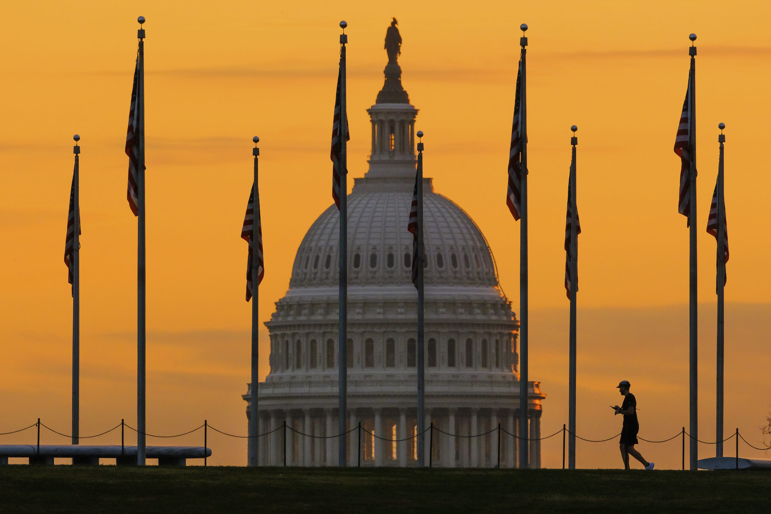 FILE - An early morning pedestrian is silhouetted against sunrise as he walks through the American ...