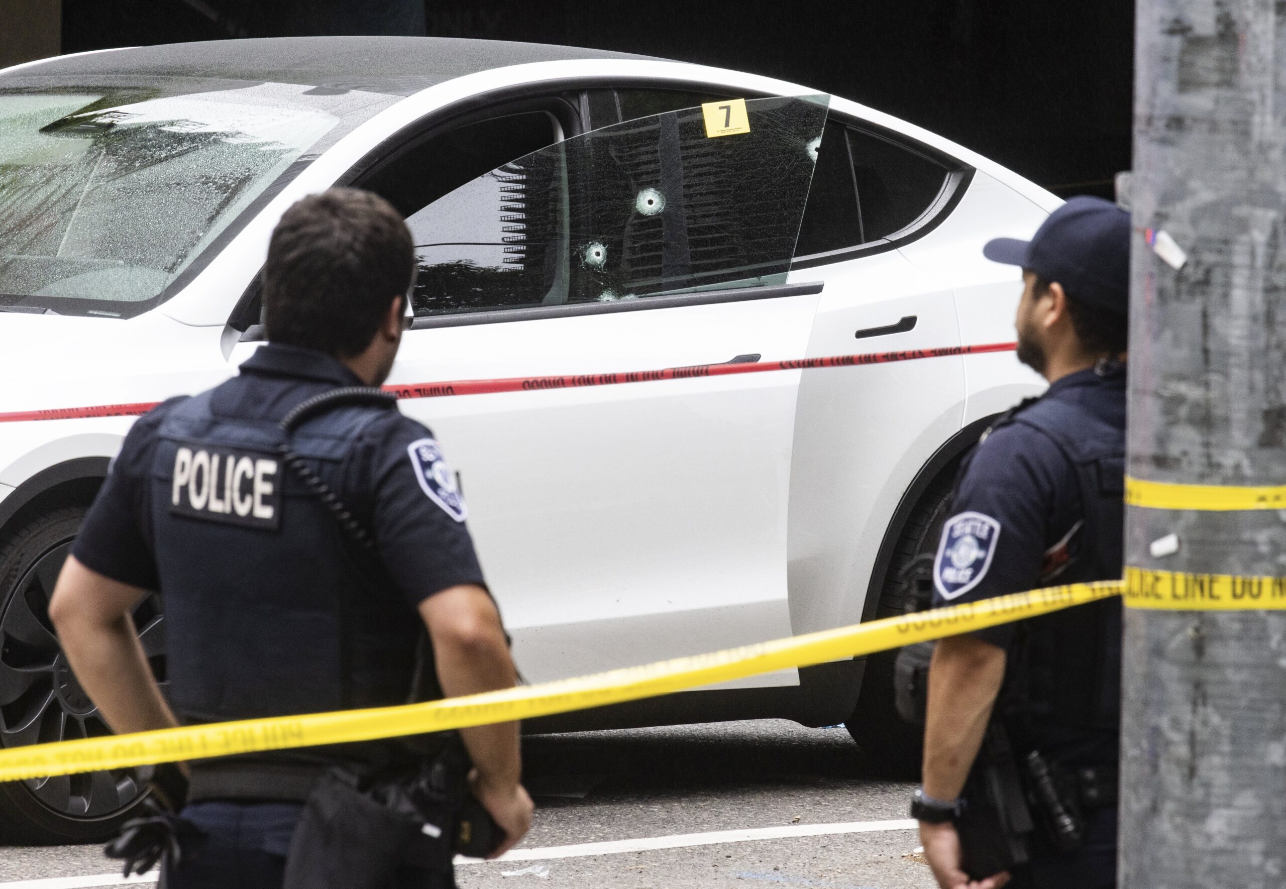Bullet holes are seen in the driver's door window of a Tesla as police secure the scene following a...