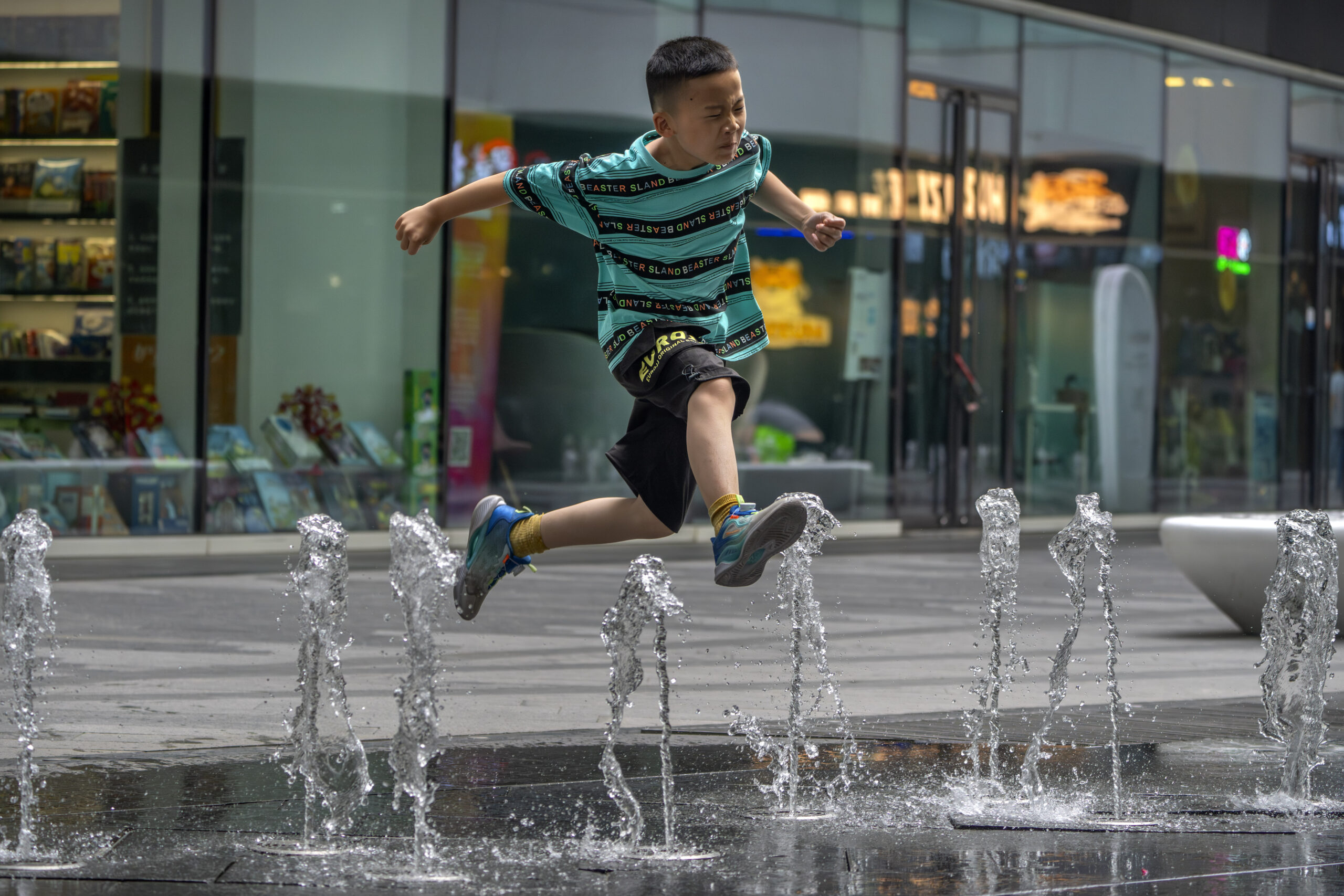 A boy leaps over a fountain at a shopping and office complex in Beijing, Saturday, July 1, 2023. An...