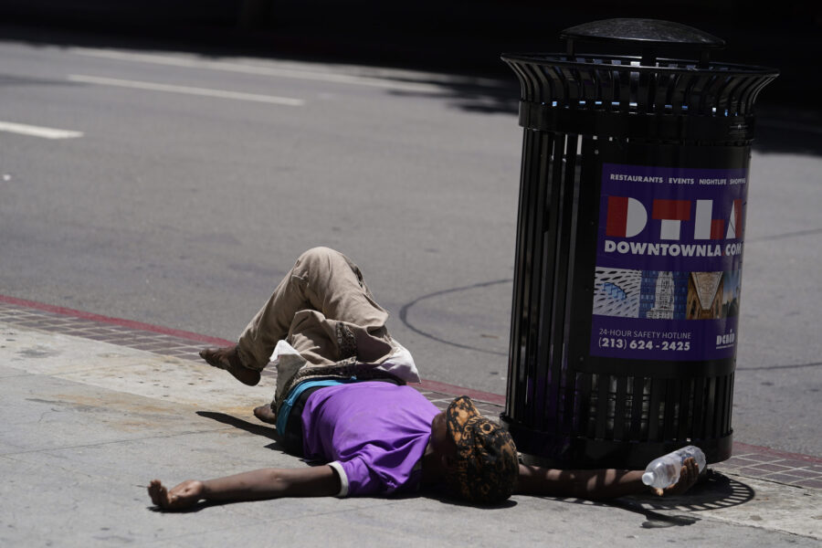 A homeless person lies on the sidewalk while holding a water bottle, in downtown Los Angeles. Exces...