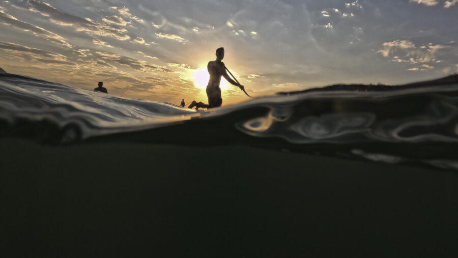 A man floats on a paddle board off Copacabana beach in Rio de Janeiro, Brazil at sunrise Thursday, ...