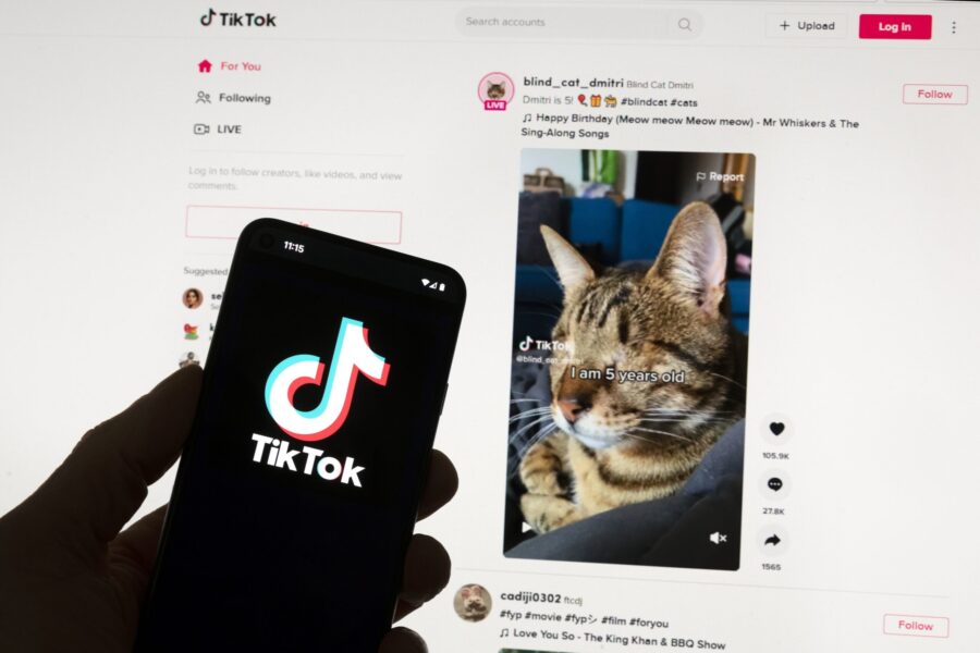 The TikTok logo is seen on a mobile phone in front of a computer screen which displays the TikTok h...
