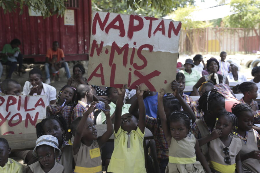 El Roi Academy students hold up a sign that reads in Creole "We are waiting for Madame Alix," durin...