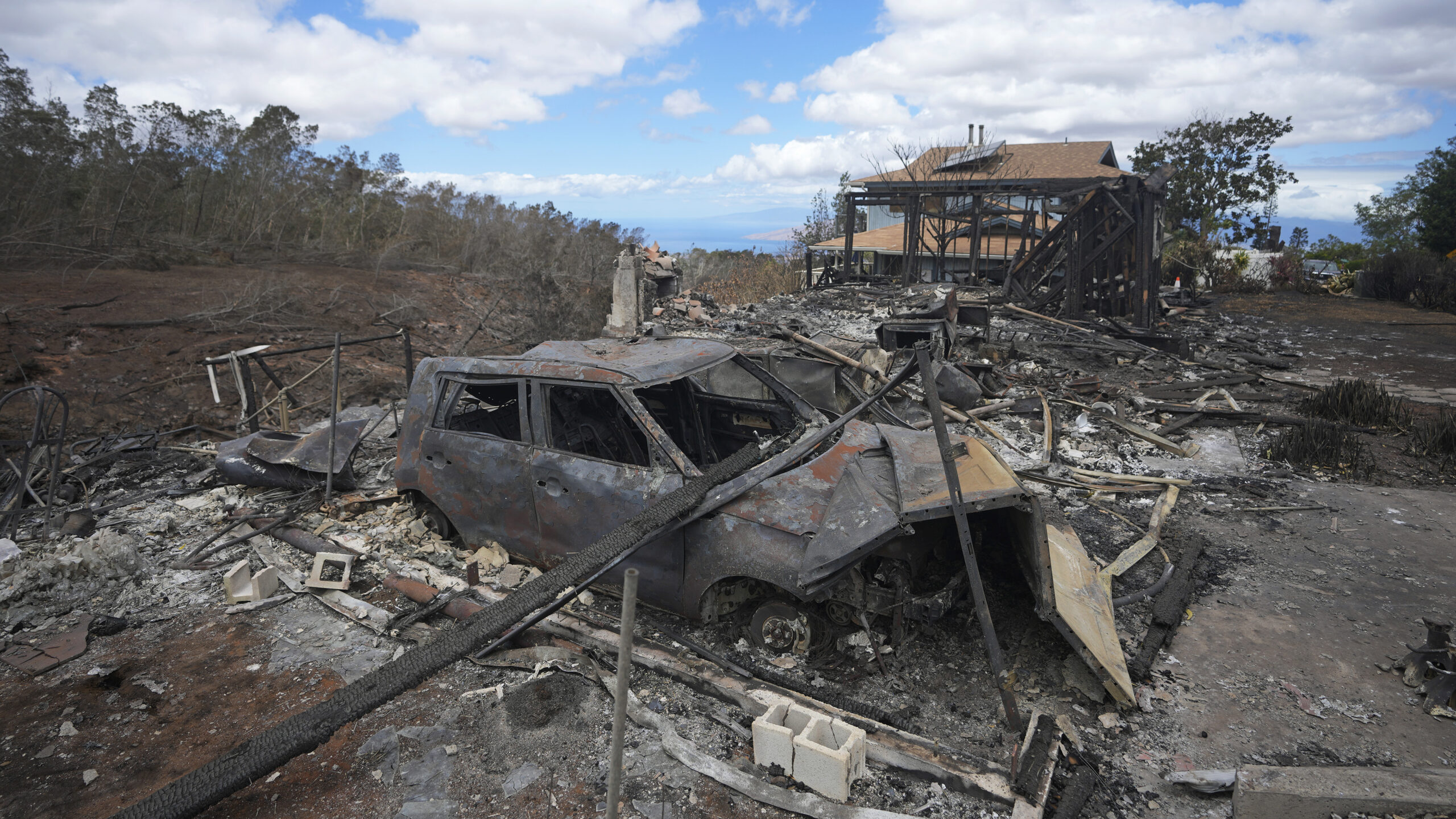 The charred remains of a vehicle sit near a wildfire-destroyed home Monday, Aug. 14, 2023, in Kula,...