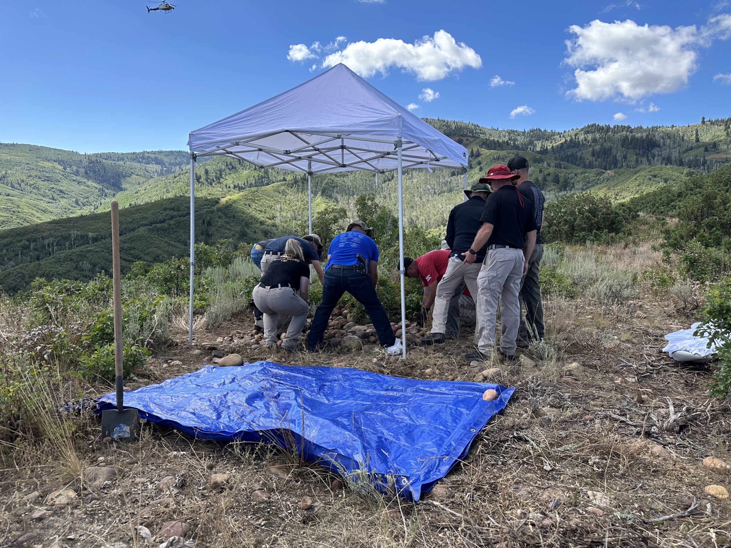 law enforcement gathered around a possible mountain gravesite in brush on a mountain top...