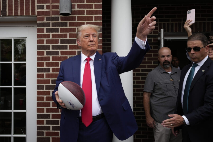 Former President Donald Trump holds a football before throwing it to the crowd during a visit to th...