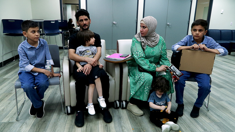 A father, mother and four young children sit in a room facing the photographer...
