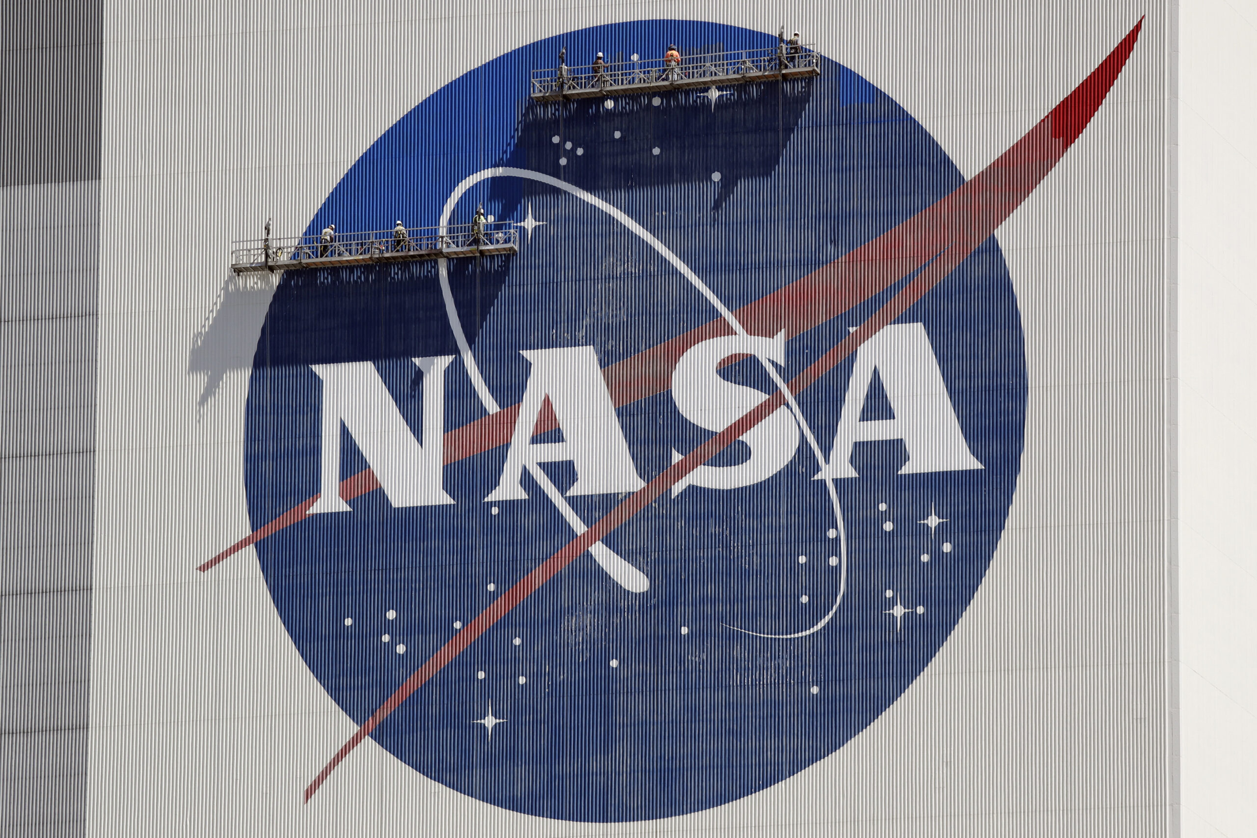 FILE - Workers on scaffolding repaint the NASA logo near the top of the Vehicle Assembly Building a...