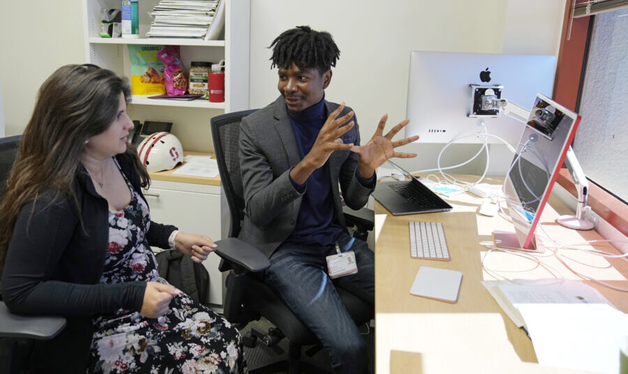 Post-doctoral researcher Tofunmi Omiye, right, gestures while talking in his office with assistant ...