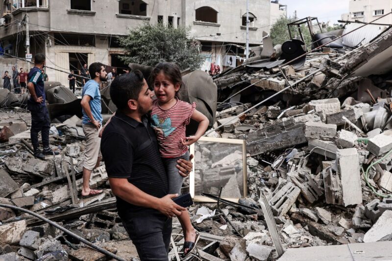 A man carries a crying child as he walks in front of a building destroyed in an Israeli air strike in Gaza City. (Mohammed Abed/AFP/Getty Images)