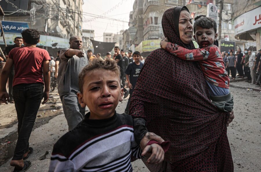 A woman and children, all injured, try to get to the safety amid destruction and chaos caused by Is...