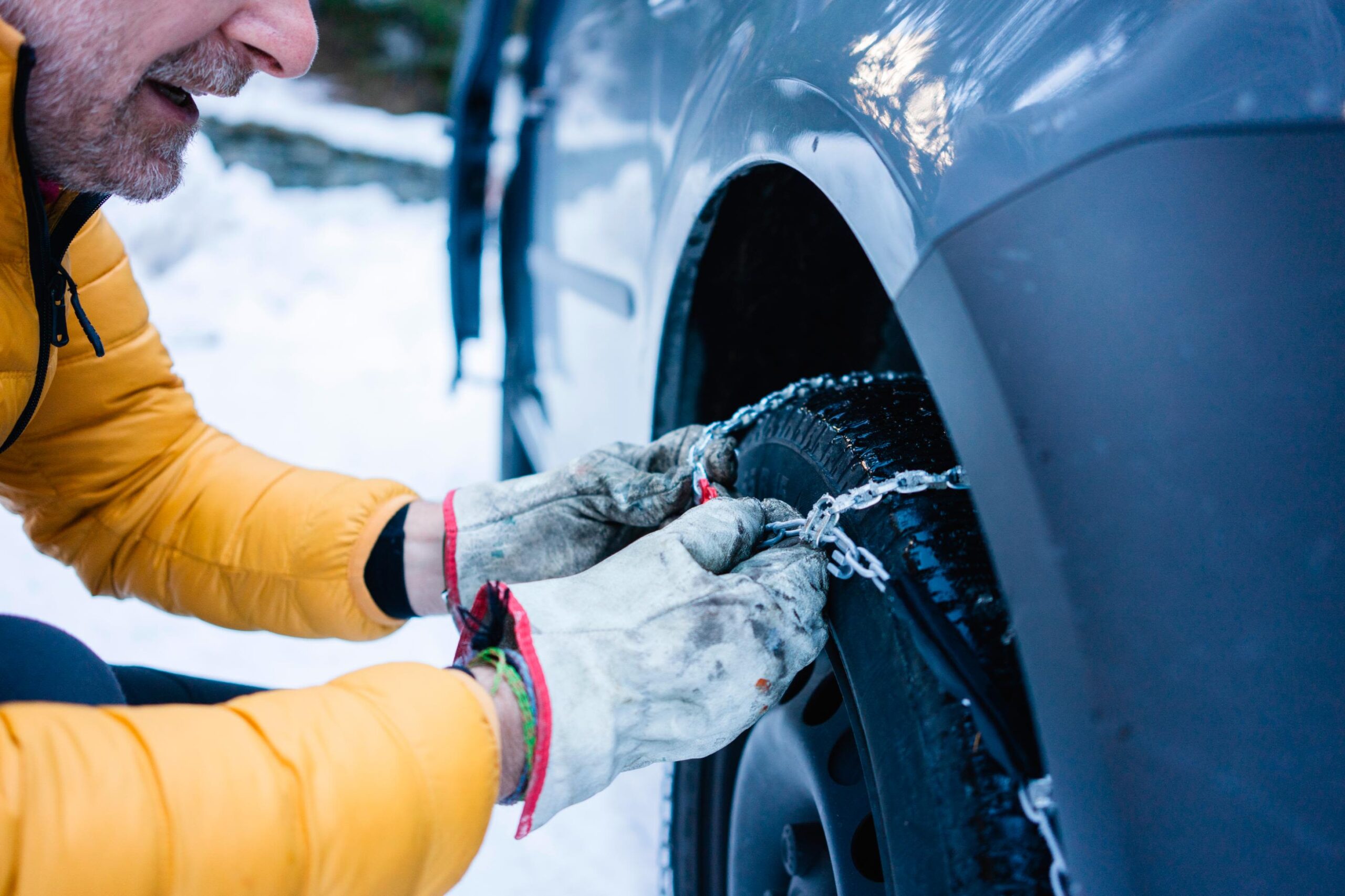 A person puts snow chains on a tire while parked in snowy conditions.
(Westend61, Getty Images)...