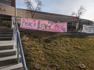 A banner outside of the school saying "Peace Love Joy." 