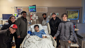 a man in a hospital bed with six friends around