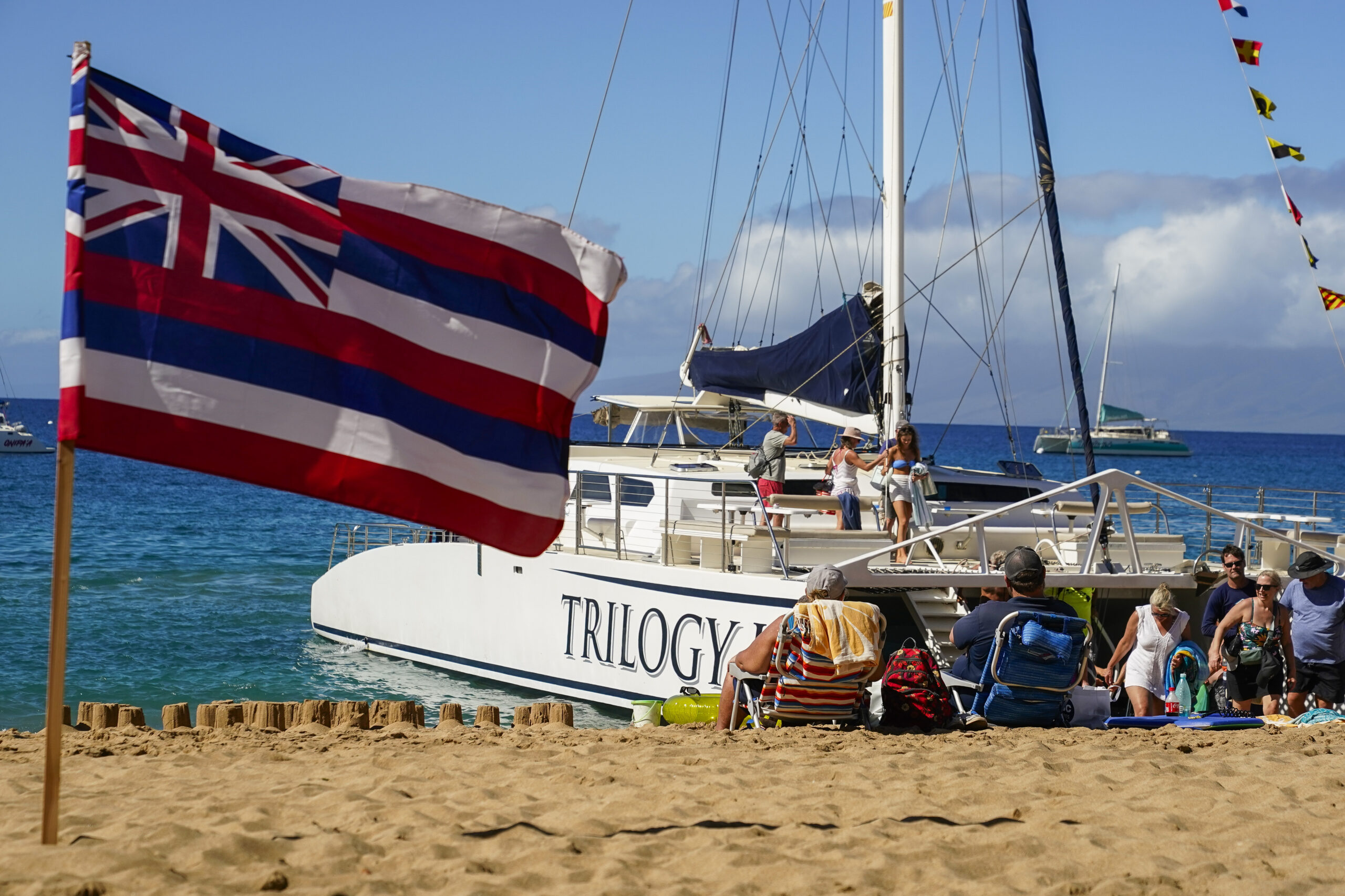 Tourists get off of a Trilogy Excursions boat arriving on Kaanapali Beach in front of a flag of Haw...