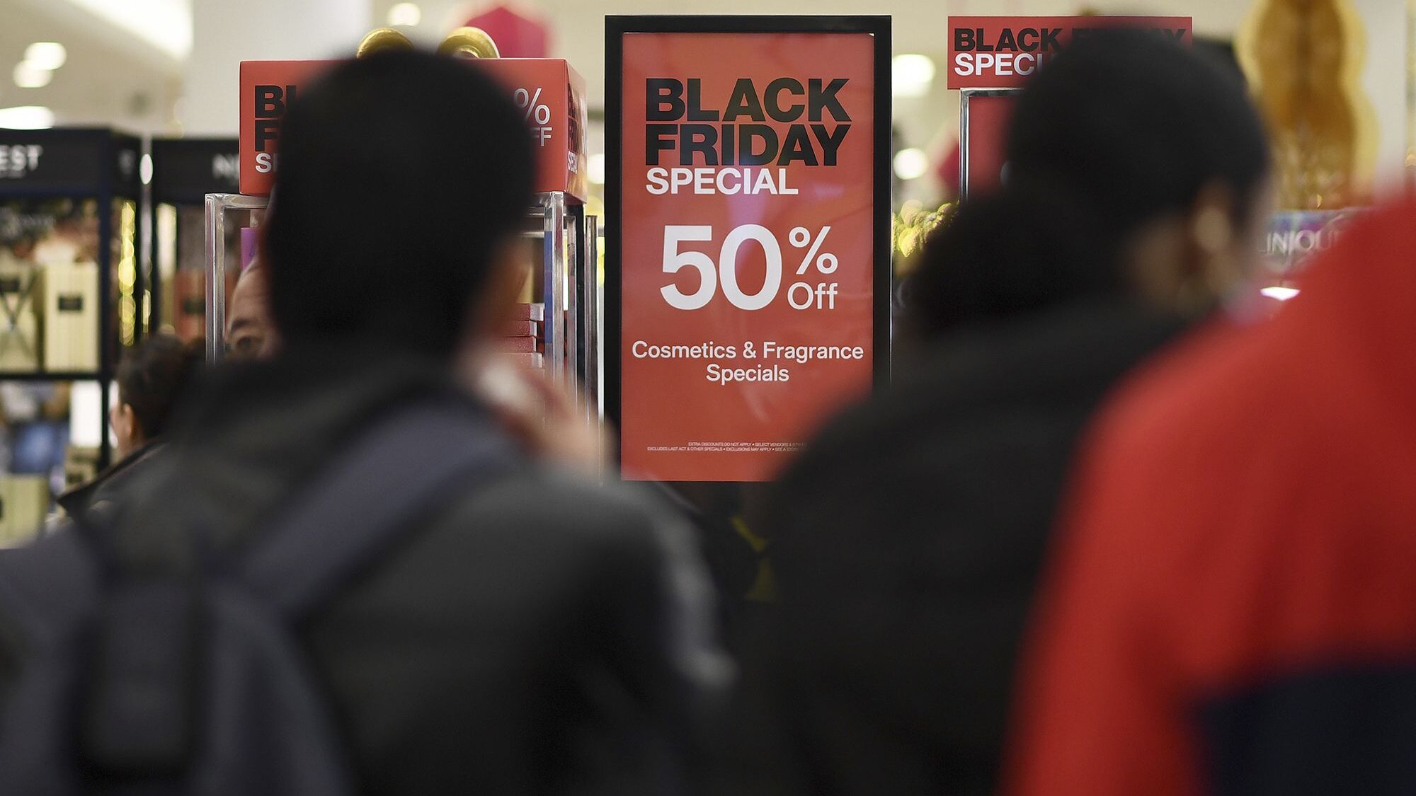 People walk past advertised Black Friday discount signs at the Macy's retail store inside the Queen...
