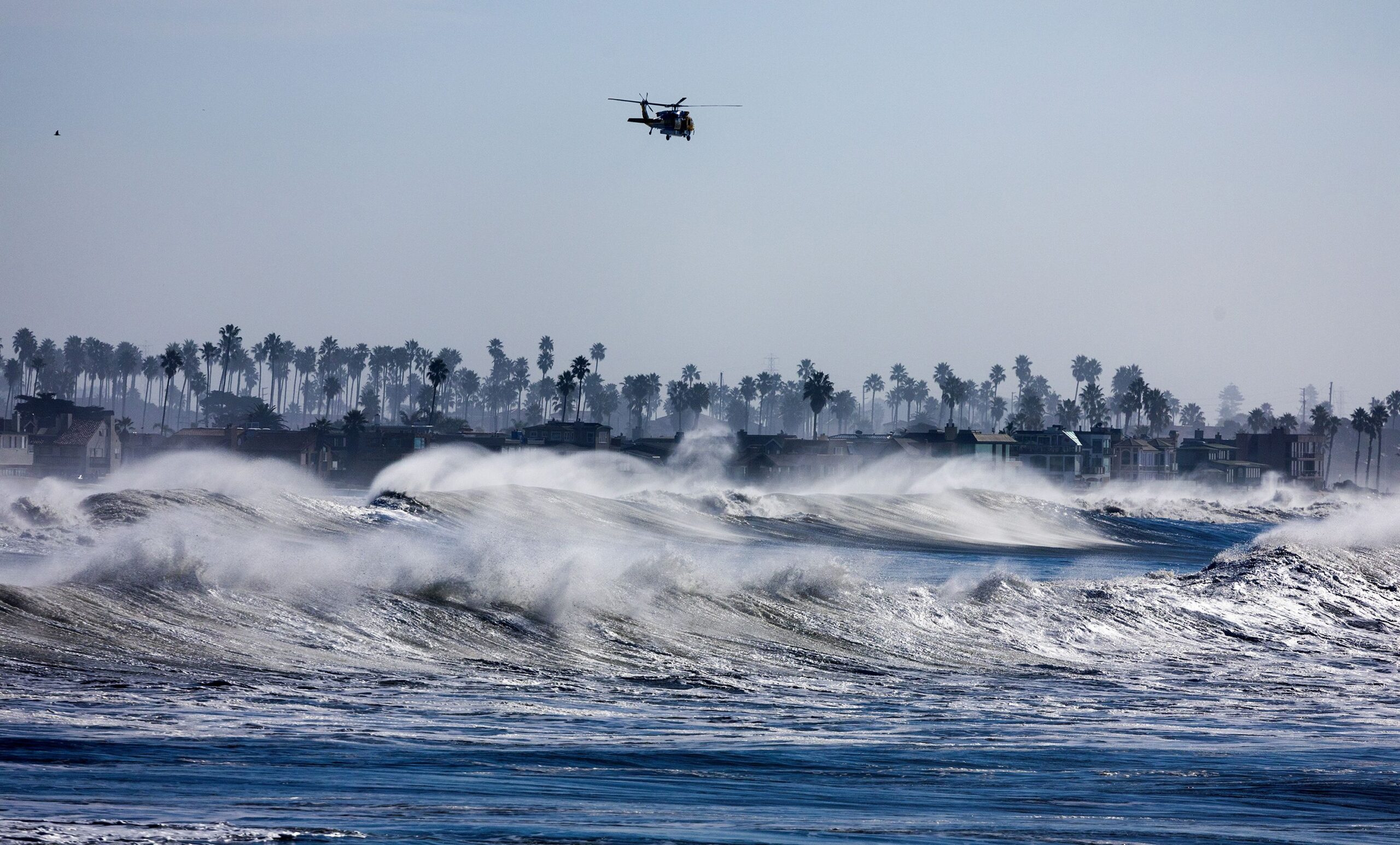 A helicopter patrols the coastline over heavy surf south of Ventura Pier on December 28. (Brian van...