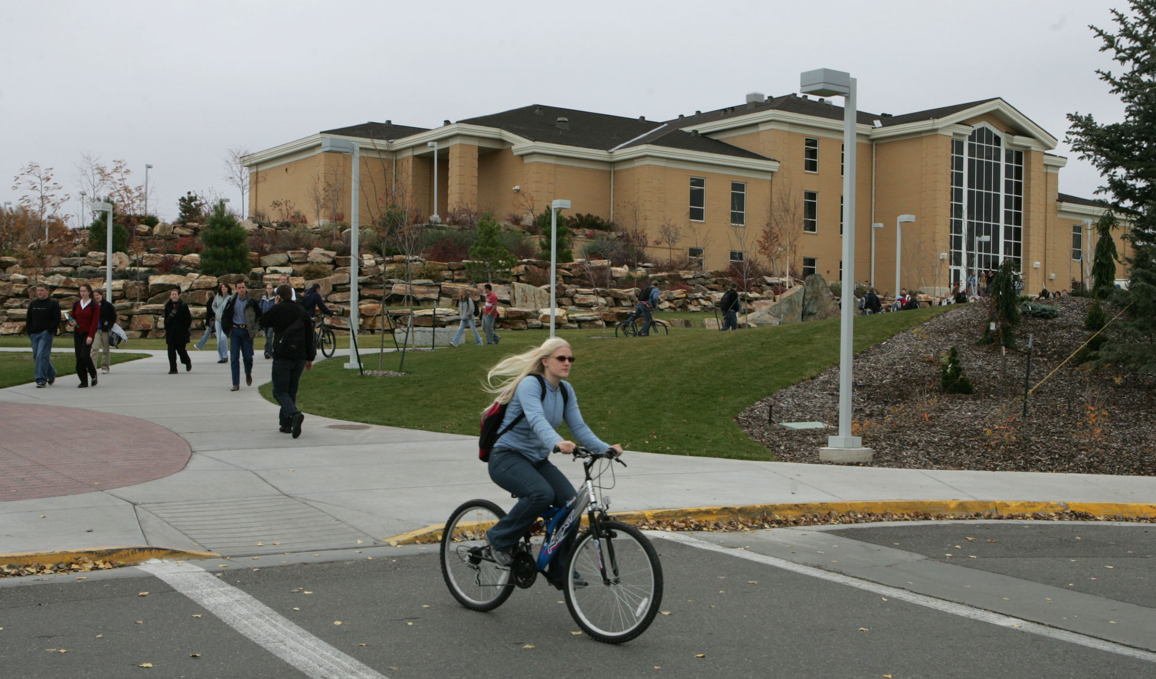 a woman rides a bike in a cross walk in front of an educational building...