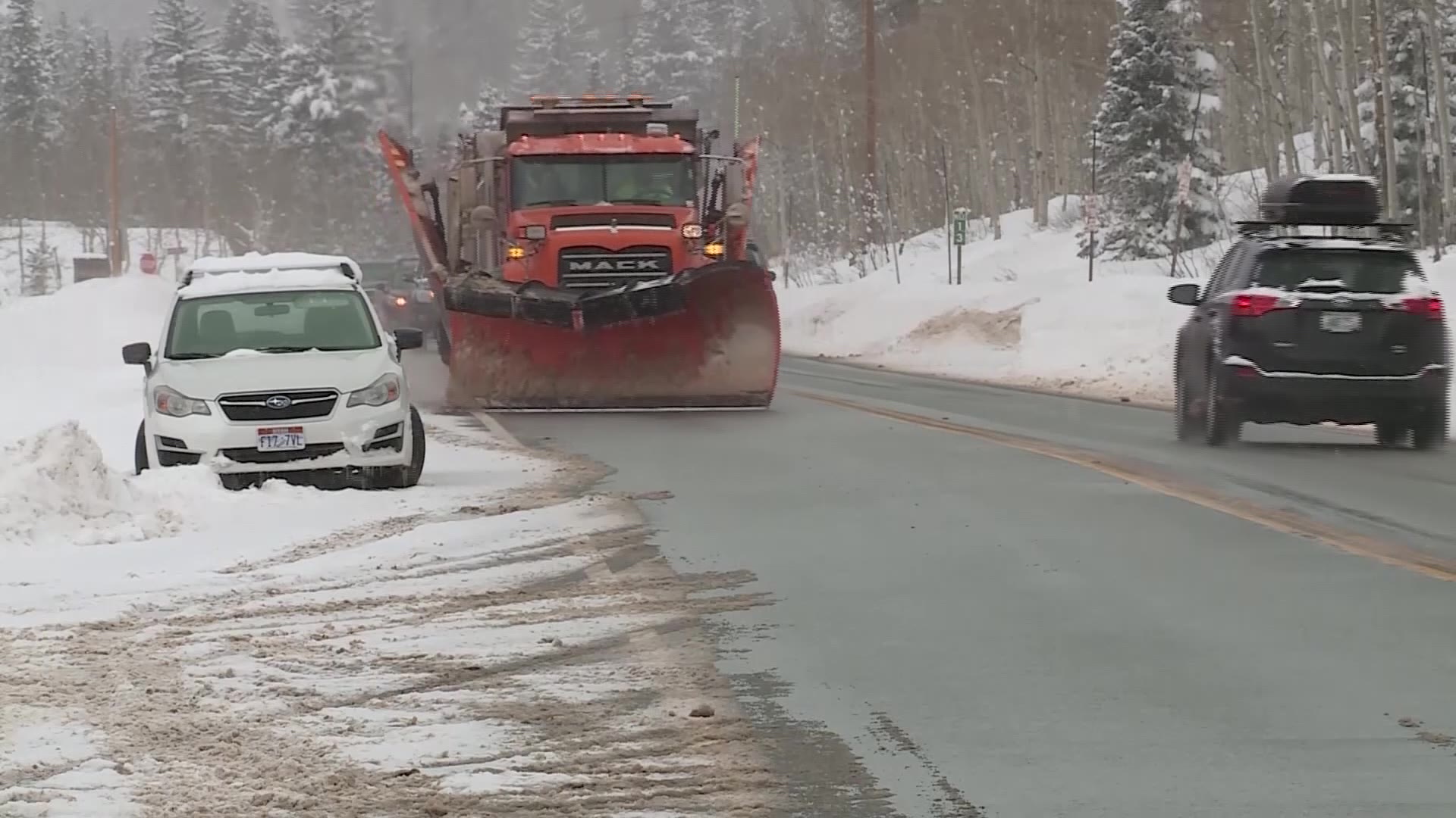 A snowplow removing snow from Big Cottonwood Canyon's roads with a car parked on the street....